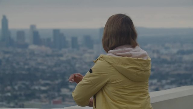 Back view of Caucasian female enjoying the view of of Los Angeles Downtown from Griffith observatory, all brand names and logos removed. 4K UHD