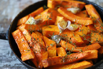 Pumpkin slices with thyme and garlic in a pan. Healthy autumn food. Vegan lunch.