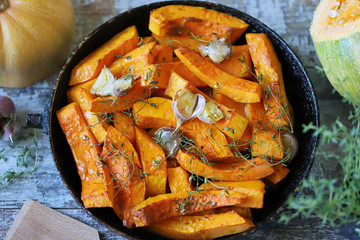 Pumpkin slices with thyme and garlic in a pan. Healthy autumn food. Vegan lunch.