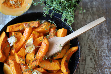 Pumpkin slices with thyme and garlic in a pan. Healthy autumn food. Vegan lunch.