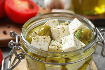 Pickled feta cheese in jar on grey table, closeup