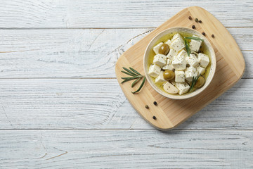 Flat lay composition with pickled feta cheese in bowl on white wooden table, space for text