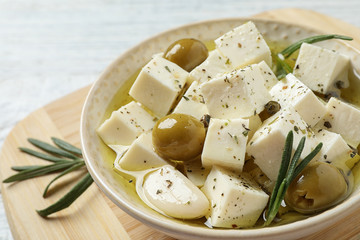 Pickled feta cheese in bowl on wooden board, closeup