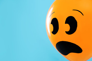 Orange balloon with drawing of scared face on blue background, space for text. Halloween party