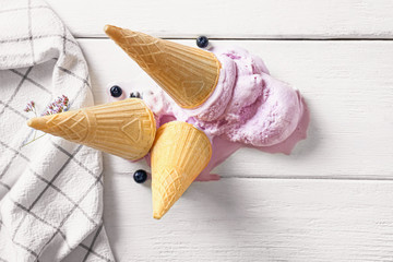 Wafer cones with tasty blueberry ice cream on white table