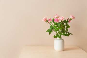 Beautiful rose flowers in vase on table against light background