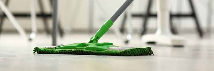 Green plastic mop cleaning laminated light dirty floor closeup
