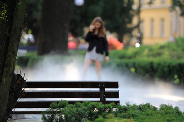 Ławka w parku i dziewczyna rozmawiająca przez telefon, mgła.