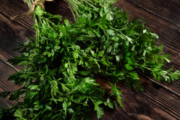 Green parsley leaves which are used as herb in kitchen, on dark wooden board