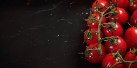 Overhead view, fresh red cherry tomatoes with green vine leaves on dark marble like board, wide...