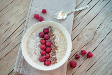 Homemade Healthy Oatmeal with Raspberries, Flax Seeds and Coconut flakes on wooden table, top view.