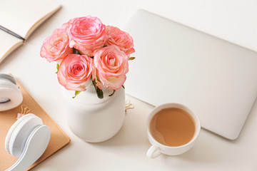 Fototapeta na wymiar Beautiful rose flowers with laptop, cup of coffee and headphones on white table
