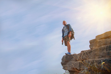 Man with backpack, traveller and explorer standing on top of mountain or cliff and looking on valley. Concept of discovery, hiking, adventure tourism and travel.
