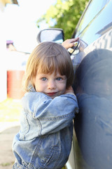 Little fashion child holds the car handle in a jeans jacket smiles and looks into the camera...
