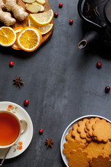 Flat lay of natural remedies for colds and flu, as well as for cozy tea drinking in cold weather, such as tea, lemon, ginger,  dried oranges, anise, Gingerbread Cookie on black stone background. 