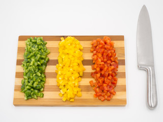 Red, green and yellow sweet bell peppers chopped on a wooden cutting board and a cutting knife