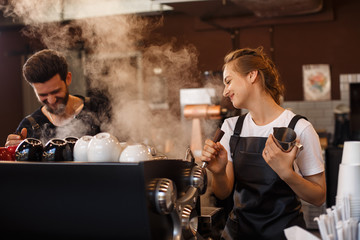 Two young smiling barista at work. Professional barista team brewing coffee using coffee machine in coffee shop. Happy young man and woman developing own coffee business. Coffee shop concept. - obrazy, fototapety, plakaty