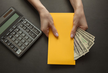 Concept of salary or bribe for work. Yellow envelope with money on a dark table.