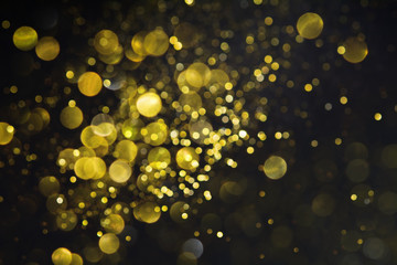 Abstract blurred glitter bokeh background in gold, on black. Festive shiny backdrop