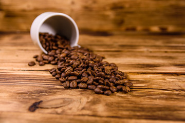 White cup and scattered coffee beans on wooden table