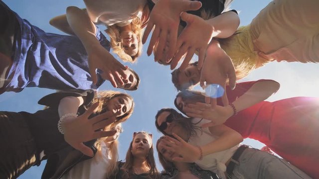 Happy friends join in a circle on a sunny day and wave their hands.
