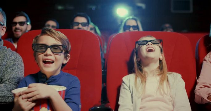 Caucasian happy and cheerful family - father, mother, son and daughter in 3D glasses laughing while sitting in the cinema with popcorn and watching comedy movie.