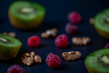 Kiwi raspberries and walnuts on a black background