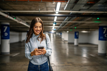 Businesswoman in Underground parking with smartphone. Young woman smiling confident at underground...