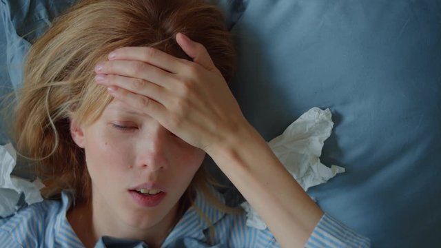 A beautiful woman having a flu being sick in bed. Her nose is stuffy, she sneezes