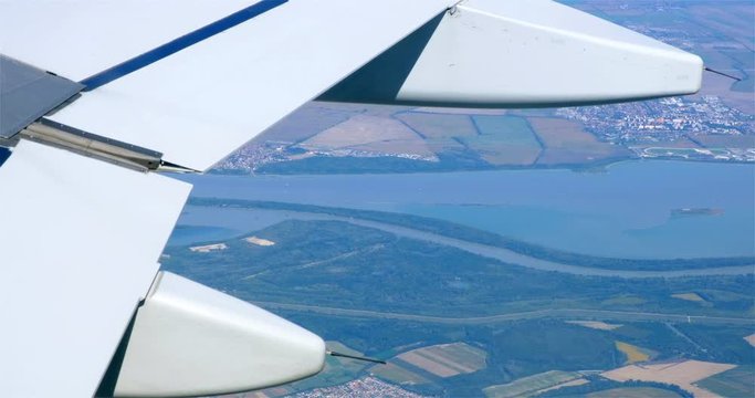 Danube river aerial view, framed by a white airplane wing in flight, at low altitude, with close up of the aircraft flaps.