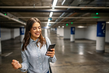 Fototapeta na wymiar Portrait of a successful businesswoman texting on the phone in underground parking. Fashionable young woman standing in a public car garage. Businesswoman in underground garage