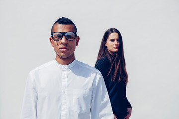 Portrait of young man with glasses and woman behind him standing in front of white background