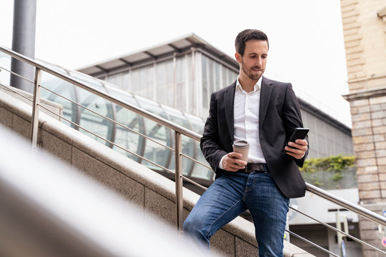 Businessman With Takeaway Coffee Using Cell Phone In The City