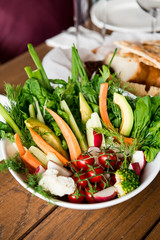 Cut vegetables on a white plate at restaurant. Fresh tomatoes, cucumbers, carrots, dill.
