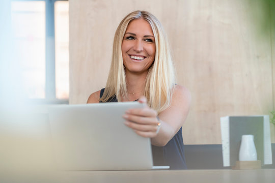 Portrait of smiling blond businesswoman with laptop in a coffee shop