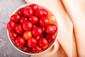 Fresh red sweet cherry in white bowl on gray and pink background. top view.