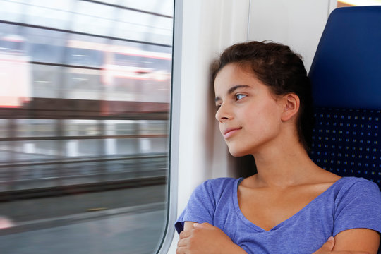 Teenage girl traveling alone by train, looking out of window