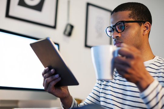 Young creative man with mini tablet having coffee break in his home office