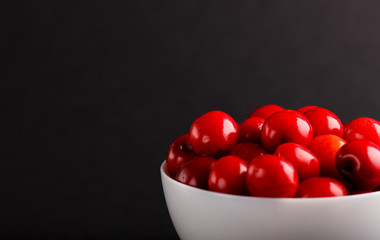 Fresh red sweet cherry in white bowl on black background. side view.