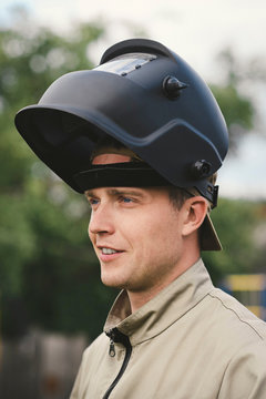 Portrait of smiling man with welding mask, standing in his backyard