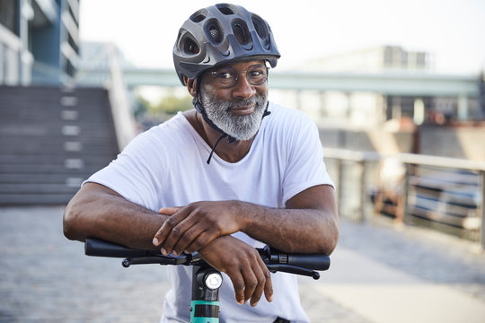 Portrait of smiling mature, man wearing cycling helmet leaning on handlebar of Electric Scooter