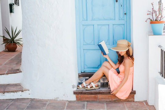 Young woman with book sitting on step of house entrance, Frigiliana, Malaga, Spain