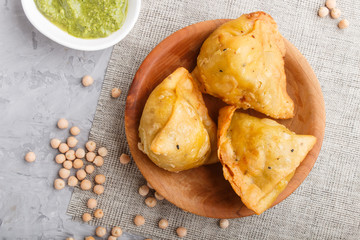 traditional indian food samosa in wooden  plate with mint chutney on a gray concrete background. top view.