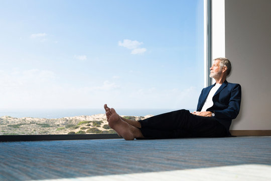 Fototapeta Senior businessman sitting at panorama window looking out