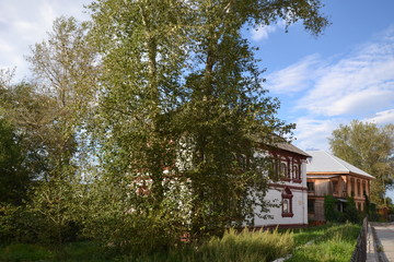 two old houses are hiding behind trees on a central street in the historic center of Solikamsk