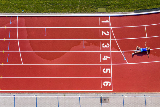 Aerial view of a young female, athlete lying on a tartan track after crossing the finishing line
