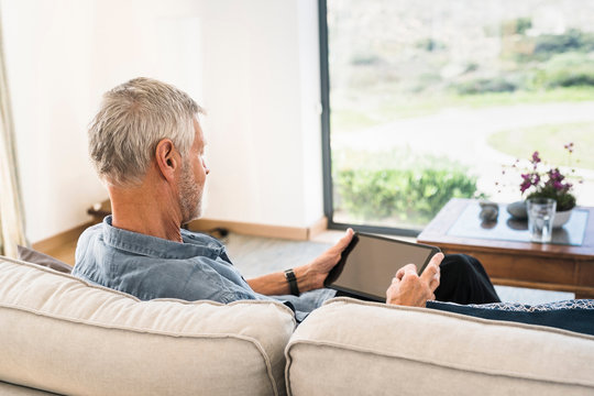 Senior man using tablet on couch at home