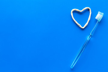 Teeth care. Heart drawn with toothpaste near toothbrushes on blue background top view space for text