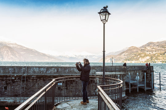 Man using mobile phone taking photos at Lake Como in winter, Italy