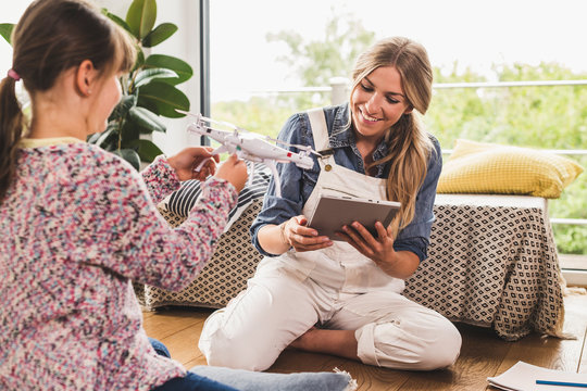 Smiling mother and daughter with tablet and drone at home